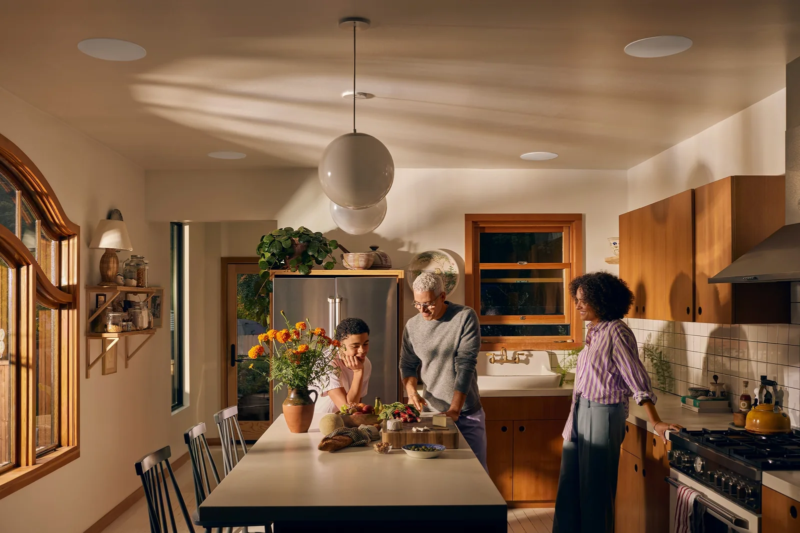 Family cooking beneath Sonos and Sonance in-ceiling speakers in a kitchen